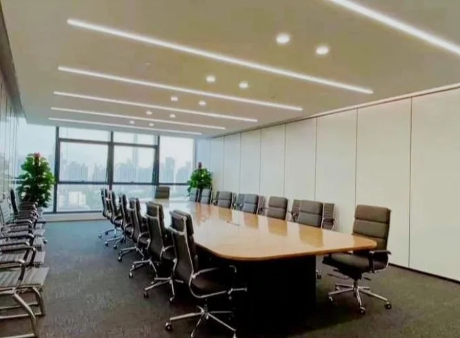Large boardroom with a long polished conference table, executive chairs, floor-to-ceiling glazing on two sides and linear ceiling lighting